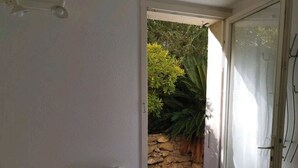 A bedroom with a bed, a radiator, and a door leading to an outdoor area with a stone wall and plants. - House with view of the pines (Narbonne)