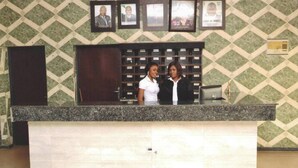 A reception desk with a patterned wall behind it, a wooden door to the left, and a computer monitor on the desk. - NAPTIN EXECUTIVE HOTEL AND SUITES  (Jos)