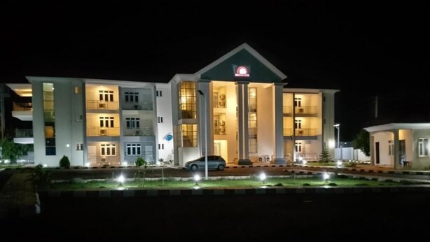 A multi-story hotel with a central entrance, large windows, and a well-lit facade at night. - NAPTIN EXECUTIVE HOTEL AND SUITES  (Jos)