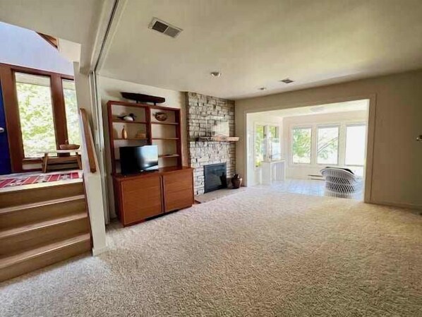 A spacious living room with a fireplace, a television on a wooden stand, and a staircase leading to another level.