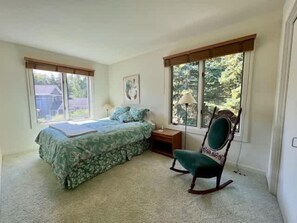 A bedroom with a bed, a rocking chair, a nightstand, and a window with a view of trees.