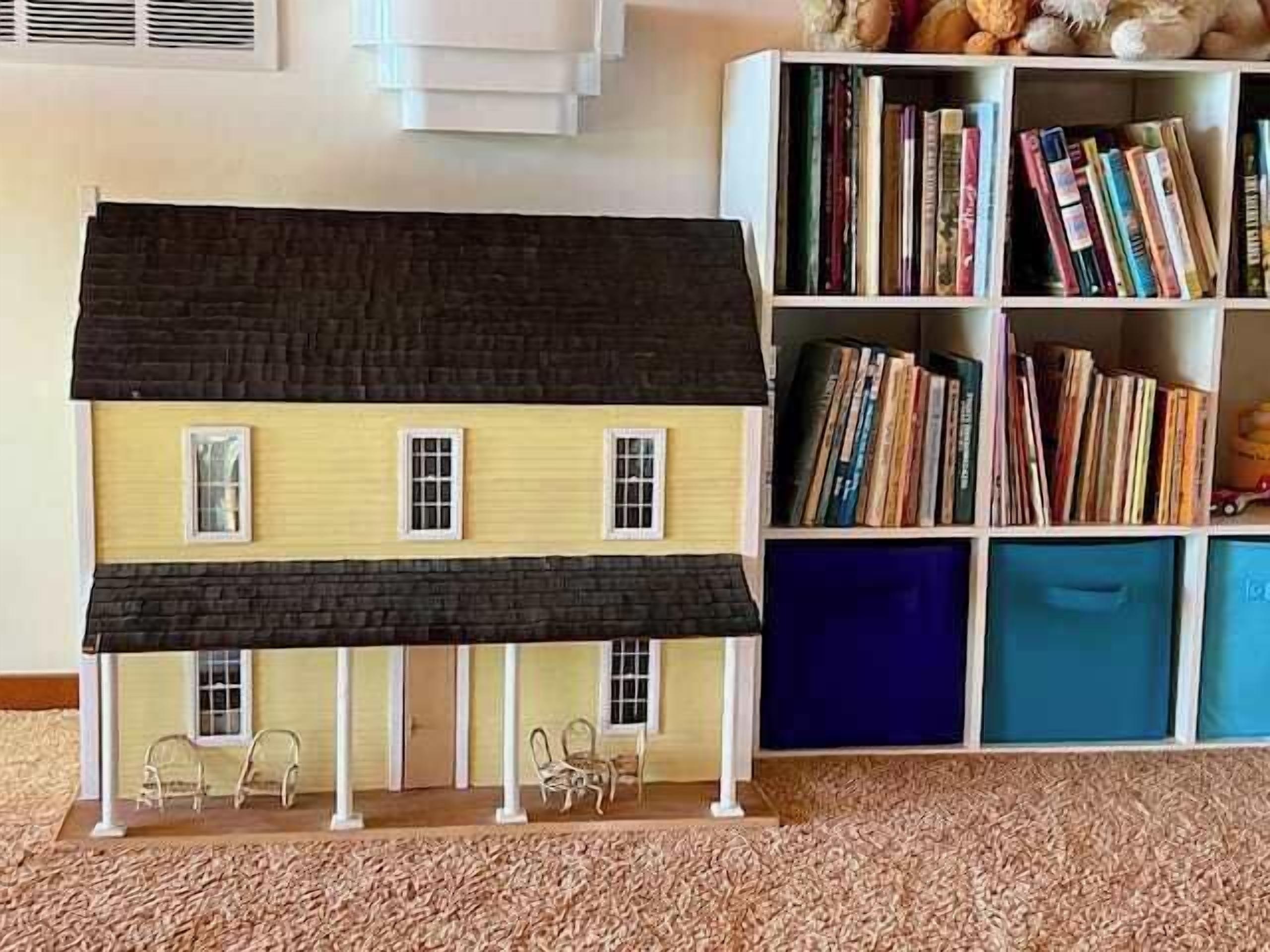 A model house with a porch, a bookshelf with books, and a carpeted floor.