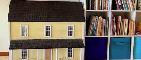 A model house with a porch, a bookshelf with books, and a carpeted floor.