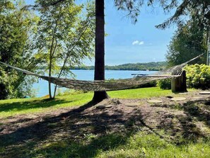 A hammock tied between two trees, a grassy area, and a body of water in the background.