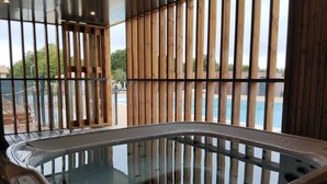 A hot tub with a view of a pool and greenery outside. - Chalet Familial Avec SPA (Saubrigues)