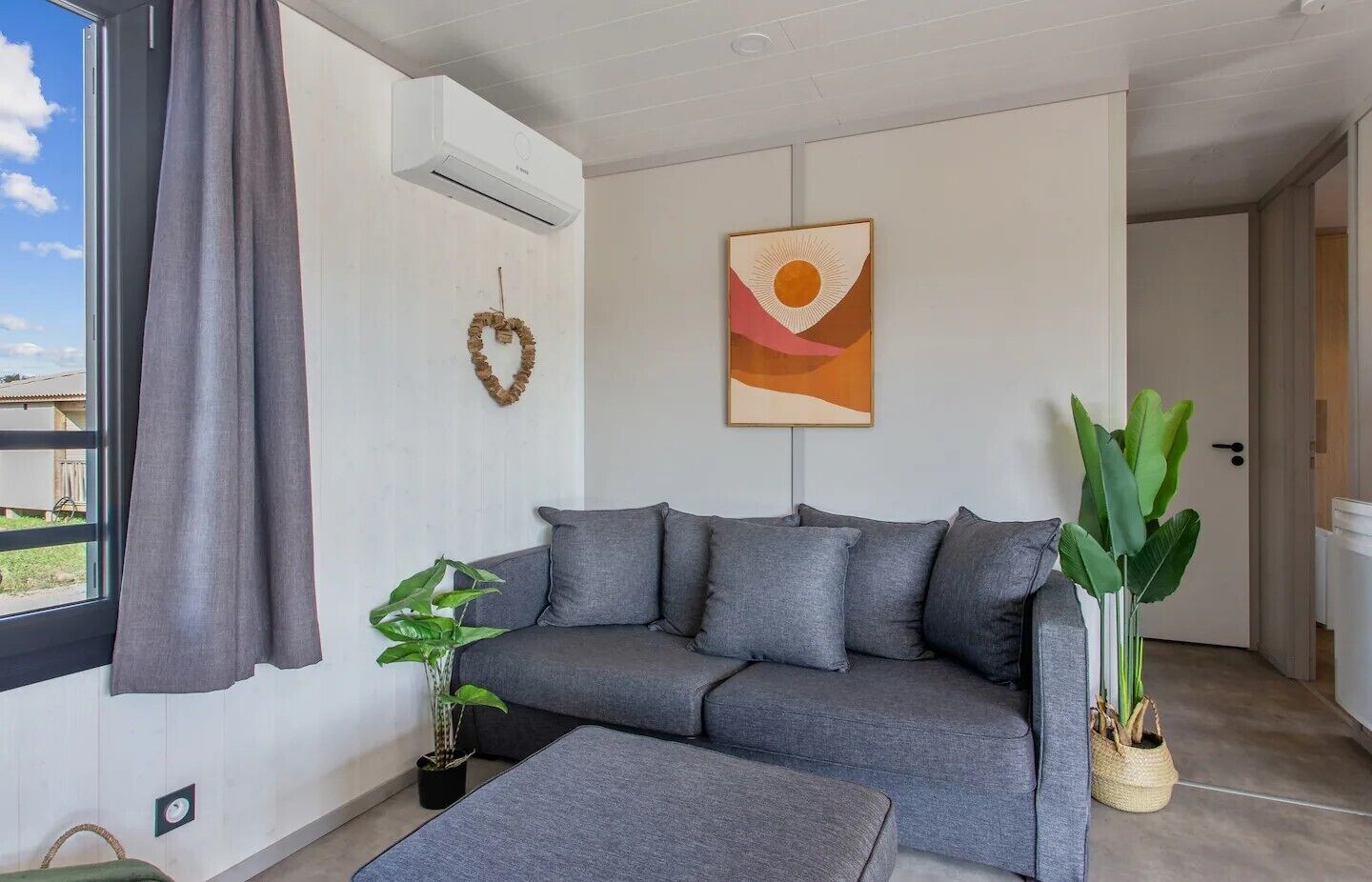 A modern living room with a grey sofa, a small table, and two potted plants.