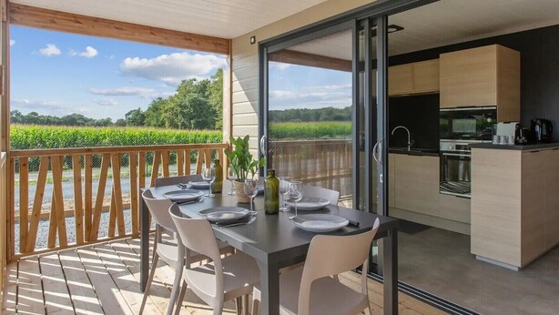 A dining area with a table set for four, a kitchen adjacent to the dining area, and a view of a green field. - Chalet Familial Avec SPA (Saubrigues)