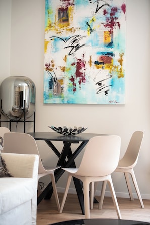 A modern dining area with a black table, two beige chairs, and a large abstract painting on the wall.