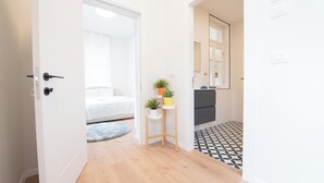 A hallway with a bed, a small table with plants, a mirror, and a patterned floor. - PORT CITY HAIFA- Authentic German Colony (Haifa)