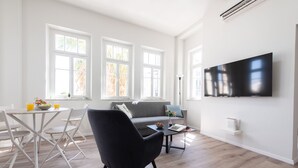 A modern living room with a flat-screen TV, a grey sofa, a black armchair, and a dining area with a white table and chairs. - PORT CITY HAIFA- Authentic German Colony (Haifa)