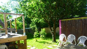 Um deck de madeira com uma mesa e cadeiras, cercado por um jardim murado com árvores e uma cerca de madeira.
