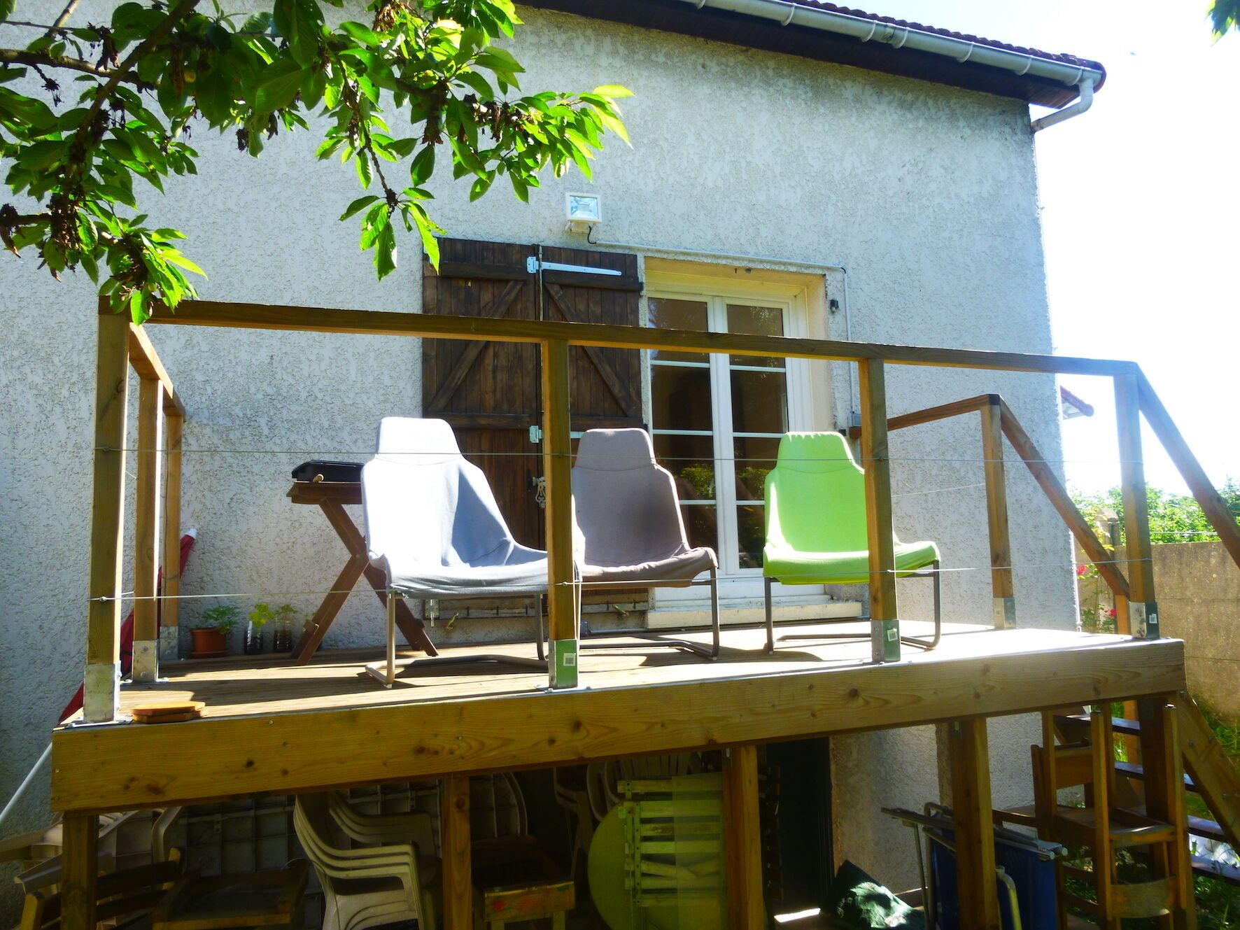 Eine Holzterrasse mit drei Stühlen und einem Tisch, mit Blick auf ein Haus mit Fenster und Tür.