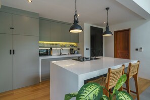 Una cocina moderna con una isla central, sillas de madera y una lámpara colgante.