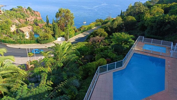Uma área de piscina com vista para o mar, cercada por vegetação exuberante e uma estrada.