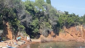 Uma praia com água cristalina, pessoas nadando e toalhas na areia.