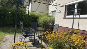 Une terrasse extérieure avec une table et des chaises, entourée de fleurs jaunes et de verdure.