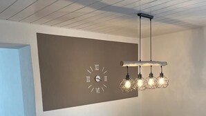 Un espace repas moderne avec une table en bois, des chaises noires et une horloge fixée au mur.