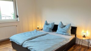Une chambre à coucher avec un lit noir, deux tables de chevet, une fenêtre et une petite table de nuit avec une lampe.