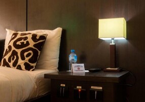 Habitación de hotel con cama, mesita de noche con lámpara, botella de agua y cartel que indica prohibido fumar.