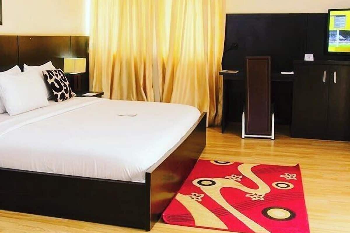 Hotellihuone, jossa on suuri sänky, työpöytä, televisio ja punakuvioinen matto.