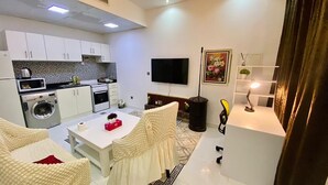 A modern living room with a white sofa, a coffee table, and a TV. There is a kitchen area with white cabinets and a microwave. - Romantic Hideaway One Bedroom Villa (Dubai)