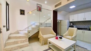 A modern living room with a staircase, two cream-colored sofas, a white coffee table, and a kitchen area with white cabinets and a tiled backsplash. - Romantic Hideaway One Bedroom Villa (Dubai)