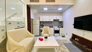 A compact living space with a sofa, a coffee table, a TV, a kitchen area, and a staircase. - Romantic Hideaway One Bedroom Villa (Dubai)