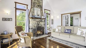 A cozy living room with a stone fireplace, a wicker chair, a sofa with decorative pillows, and a welcome sign. - Eagle's Landing: Lake Michigan Waterfront, Private Beach, Fireplace, Decking (Fennville)