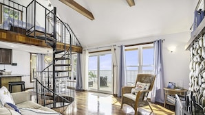 A spacious living area with a wooden staircase, a wicker chair, and a view of the outdoors. - Eagle's Landing: Lake Michigan Waterfront, Private Beach, Fireplace, Decking (Fennville)