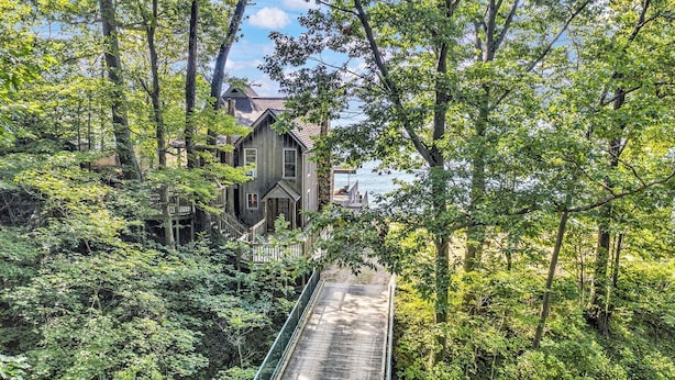 A wooden house surrounded by dense forest, connected to a dock by a wooden bridge. - Eagle's Landing: Lake Michigan Waterfront, Private Beach, Fireplace, Decking (Fennville)