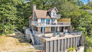 A two-story house with a balcony, a stone chimney, and a deck with outdoor furniture. - Eagle's Landing: Lake Michigan Waterfront, Private Beach, Fireplace, Decking (Fennville)