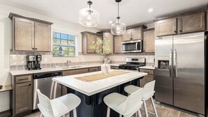 A modern kitchen with a central island, stainless steel appliances, and pendant lighting.