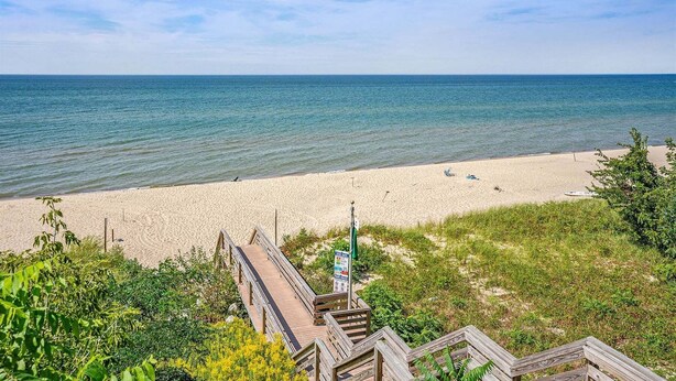 A beach with a wooden boardwalk leading to the shore, clear skies, and calm sea.