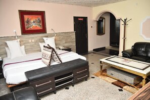 A hotel room with a bed, a desk, a chair, a coat rack, and a door. - Room-choice Gate Hotel-guest Room (Benin City)