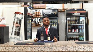 Zona de bar con mostrador, estanterías llenas de botellas y una pantalla de televisión mostrando noticias.