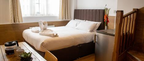 A hotel room with a bed, a small table with a plant, a refrigerator, and a wooden staircase.