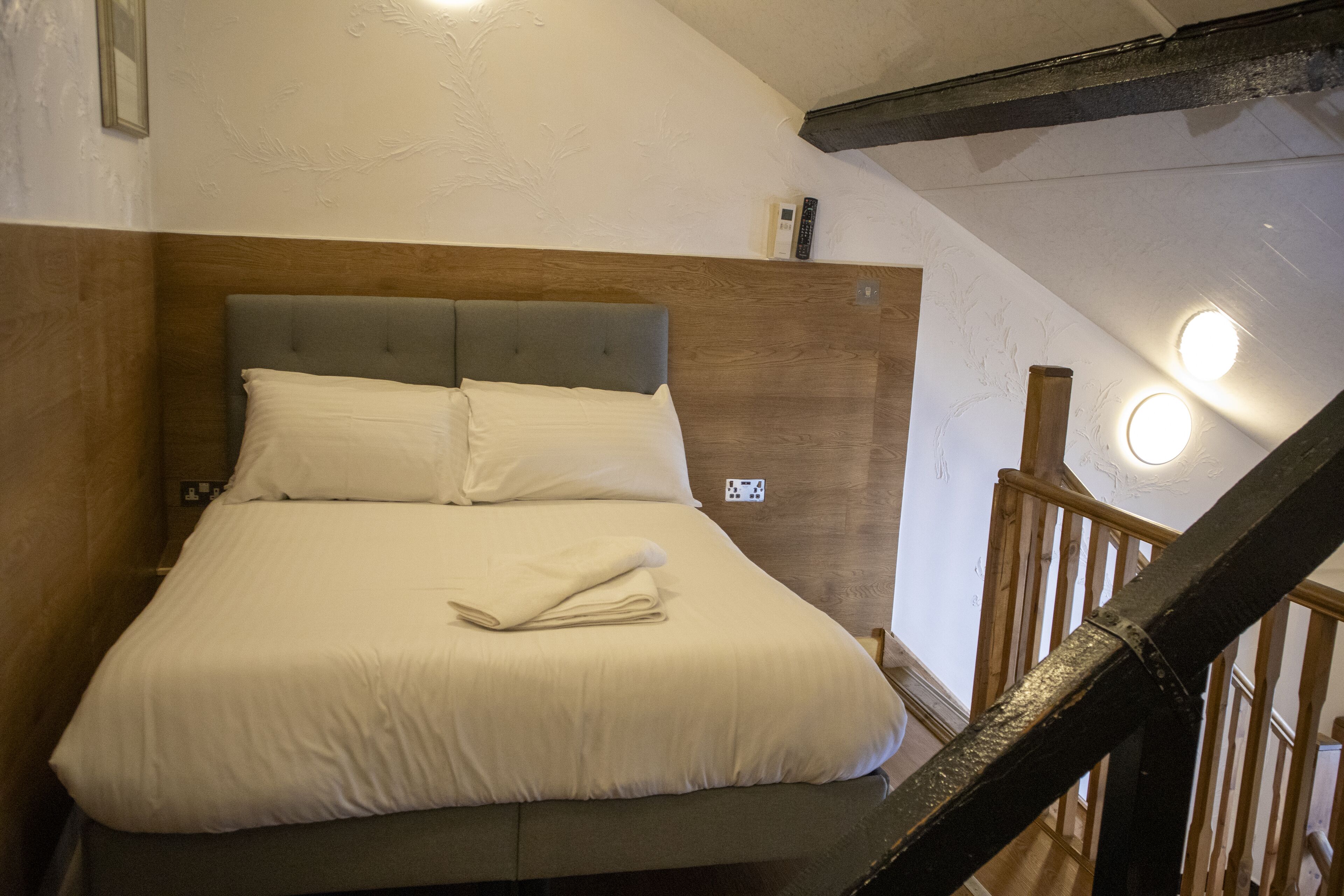 A neatly made bed with a grey headboard in a room with wooden beams and a staircase.