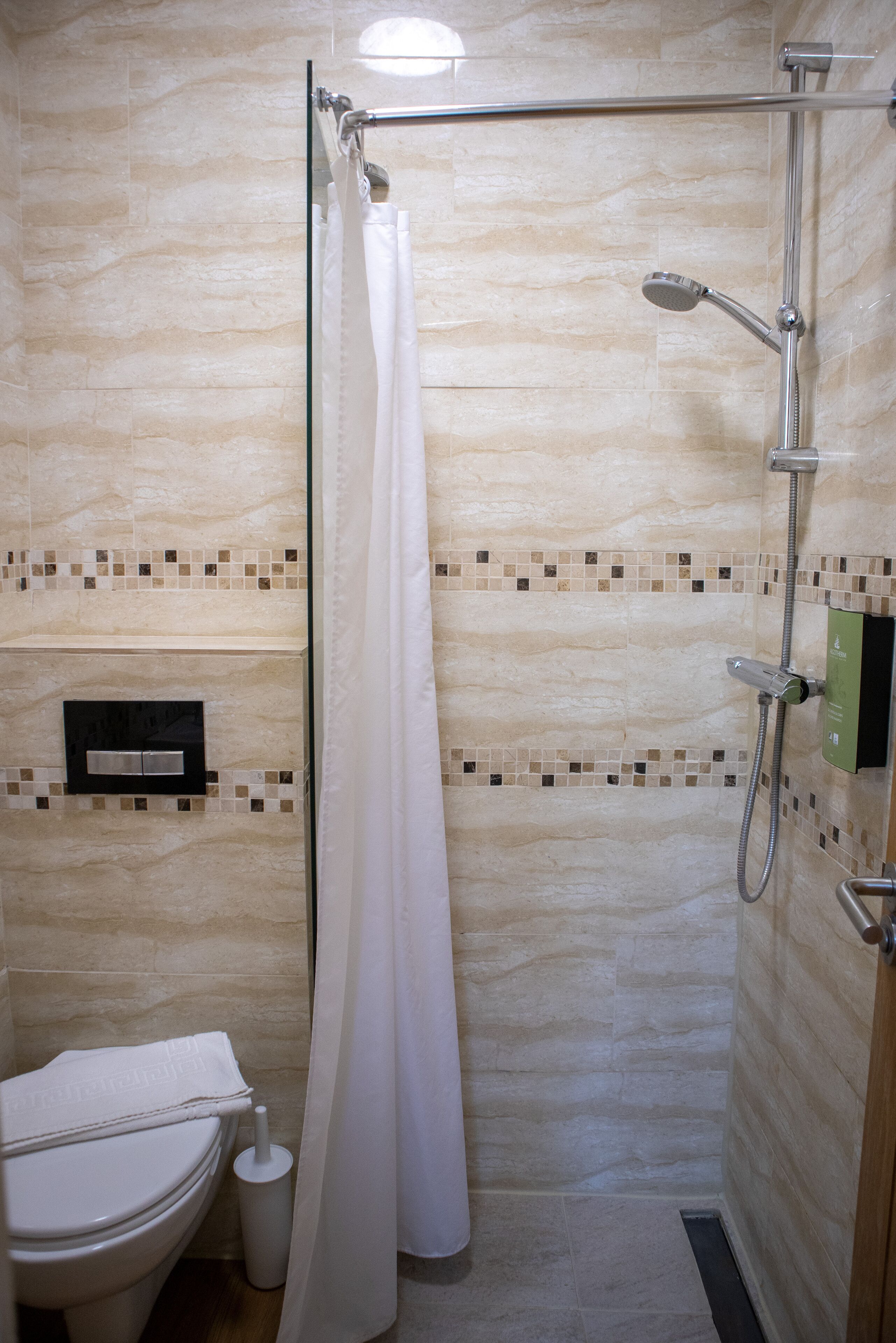 A modern bathroom with a glass shower enclosure, a toilet, and a hand dryer.