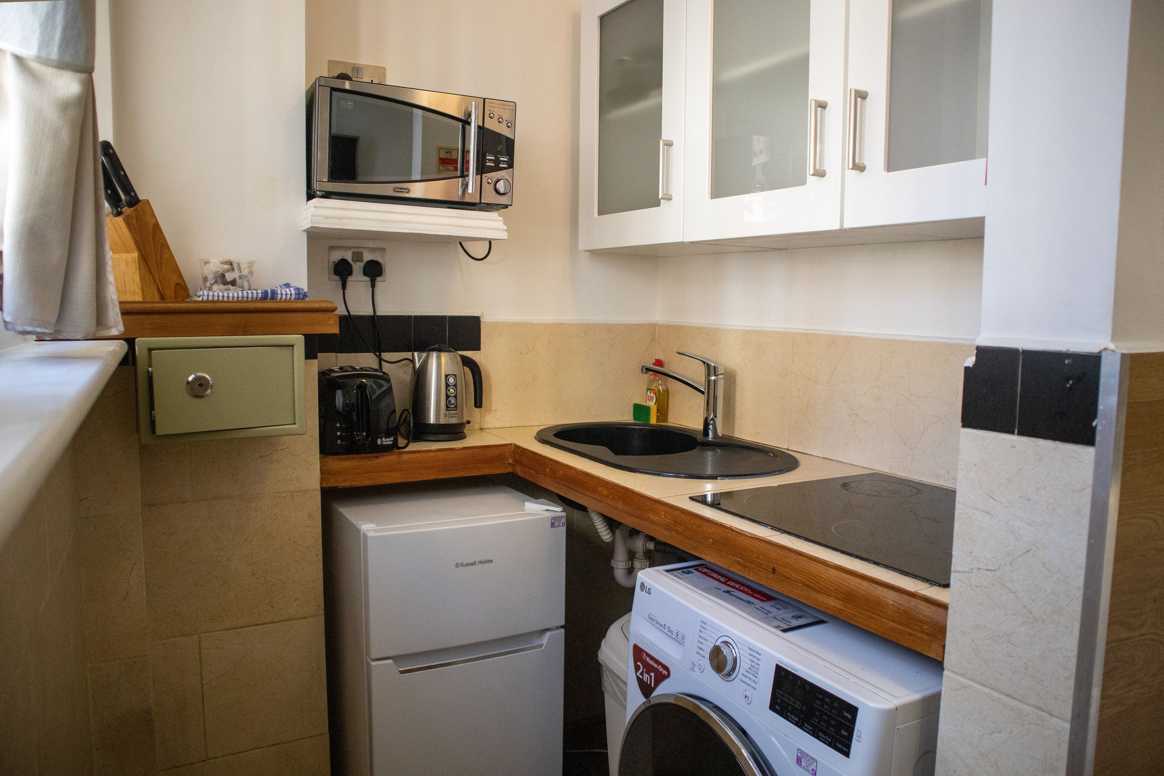 Una cocina compacta con microondas, lavamanos y lavadora.