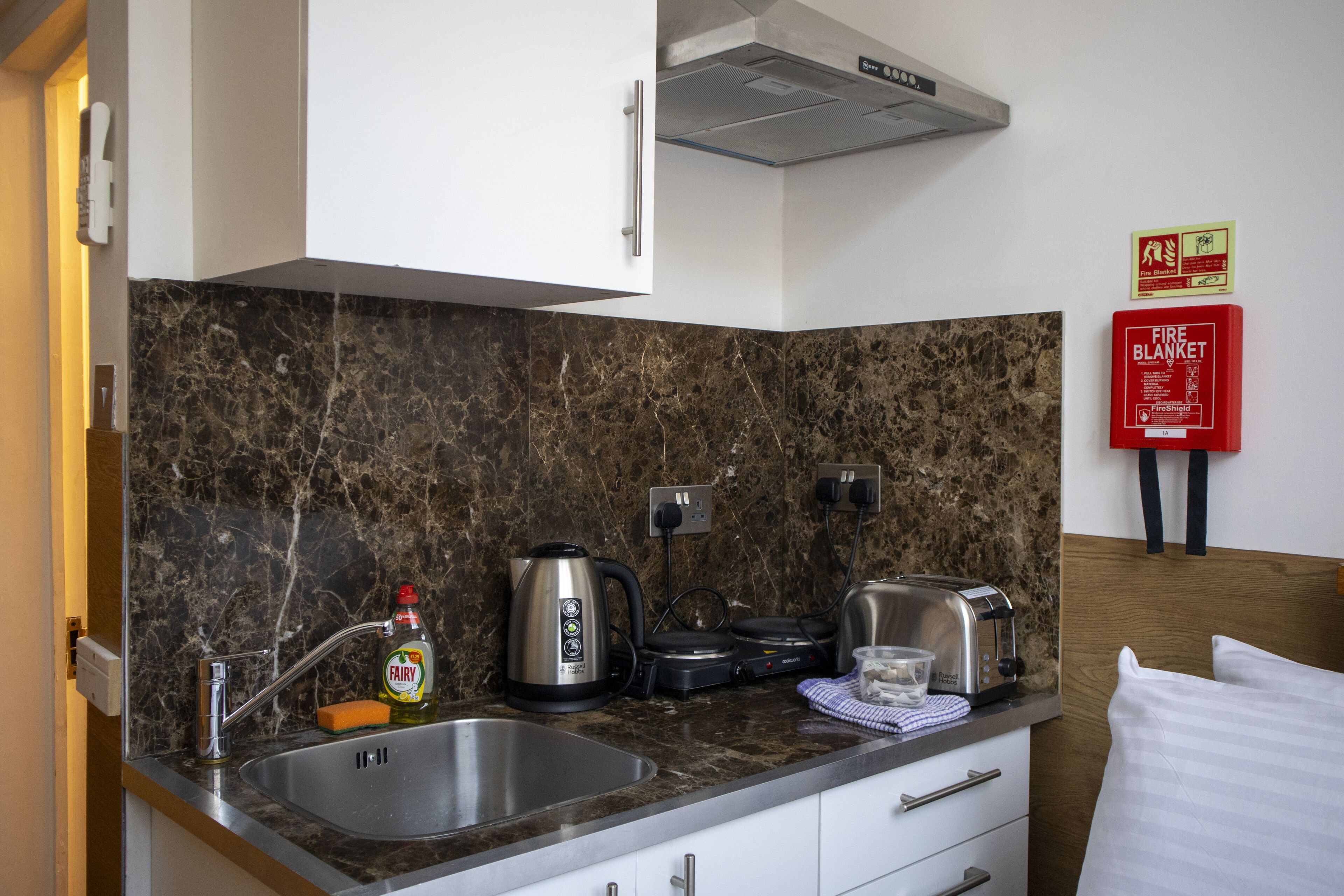 A compact kitchen with a marble backsplash, stainless steel appliances, and a fire blanket on the wall.