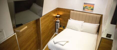 A compact hotel room with a bed, a bedside table, a lamp, and a wall-mounted TV.