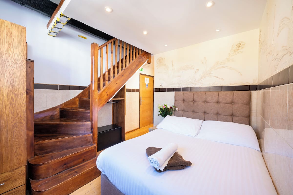 A hotel room with a wooden staircase, a bed with white linens, and a floral wall mural.