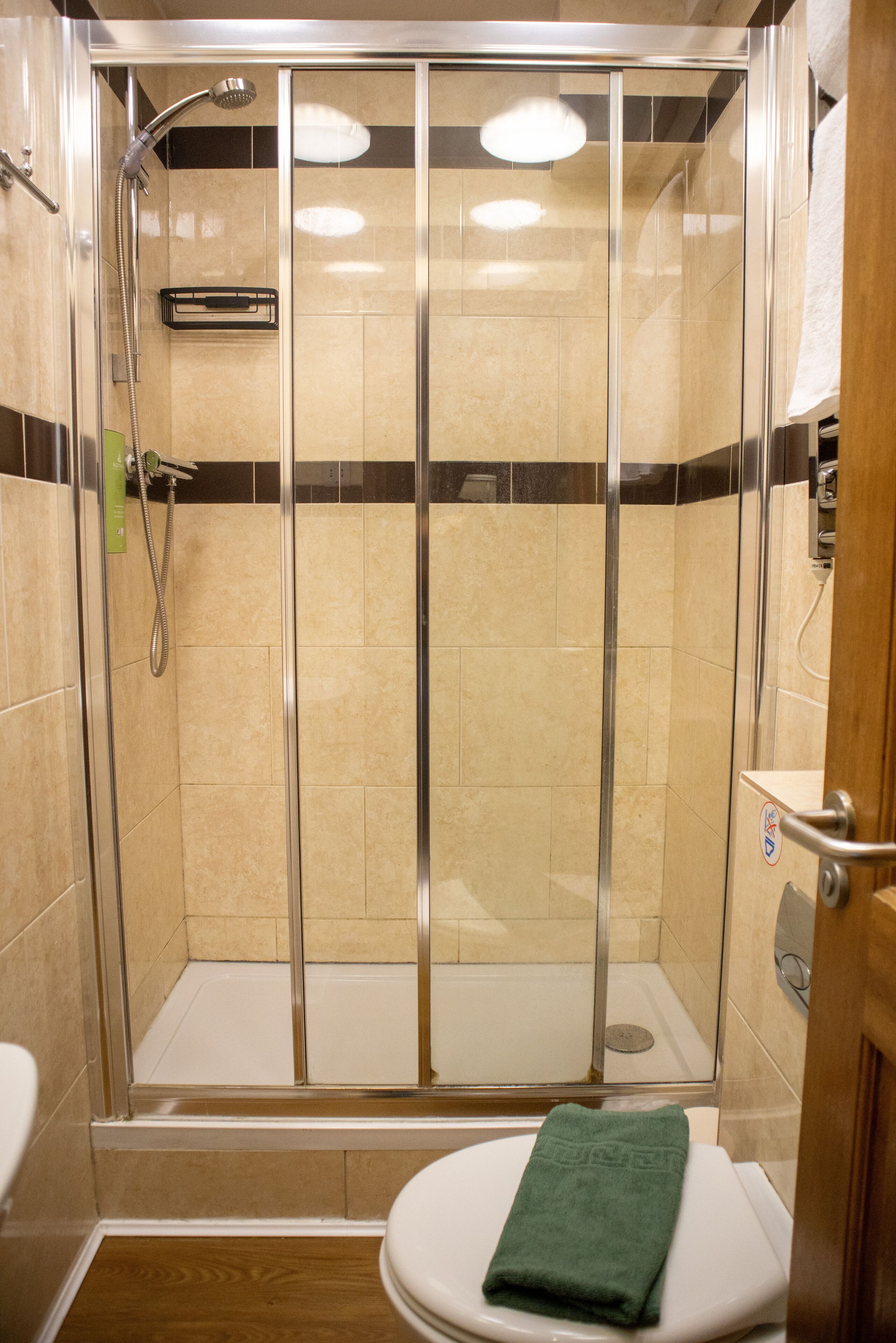 Una ducha con puerta de vidrio, un inodoro con una toalla verde y una pared de azulejos.