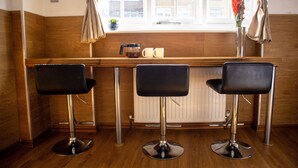 Un espace bar avec trois tabourets noirs, un appareil à café et un vase rempli de fleurs, le tout posé sur un comptoir en bois.