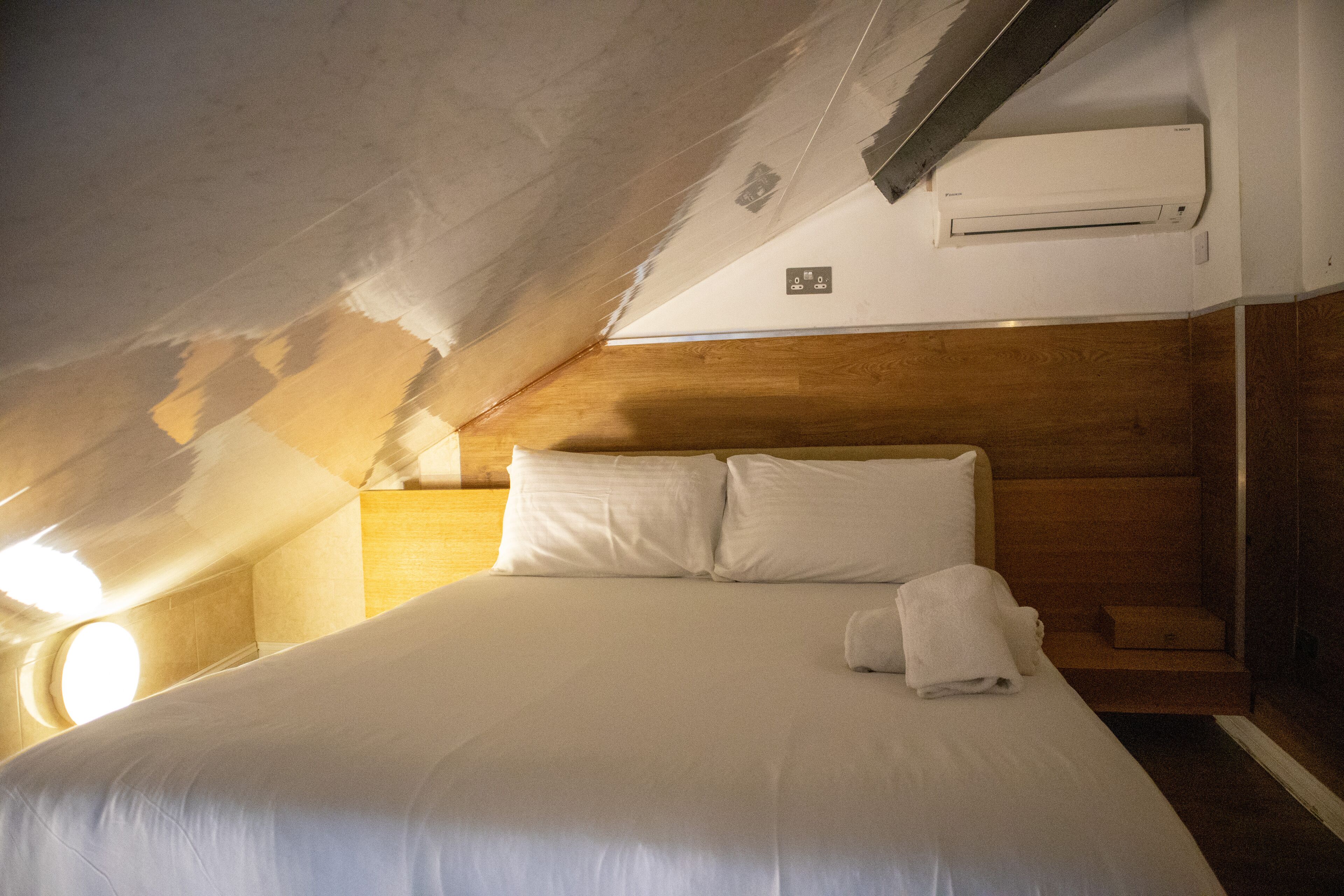 A bedroom with a wooden headboard, a large bed with white linens, and an air conditioning unit mounted on the wall.