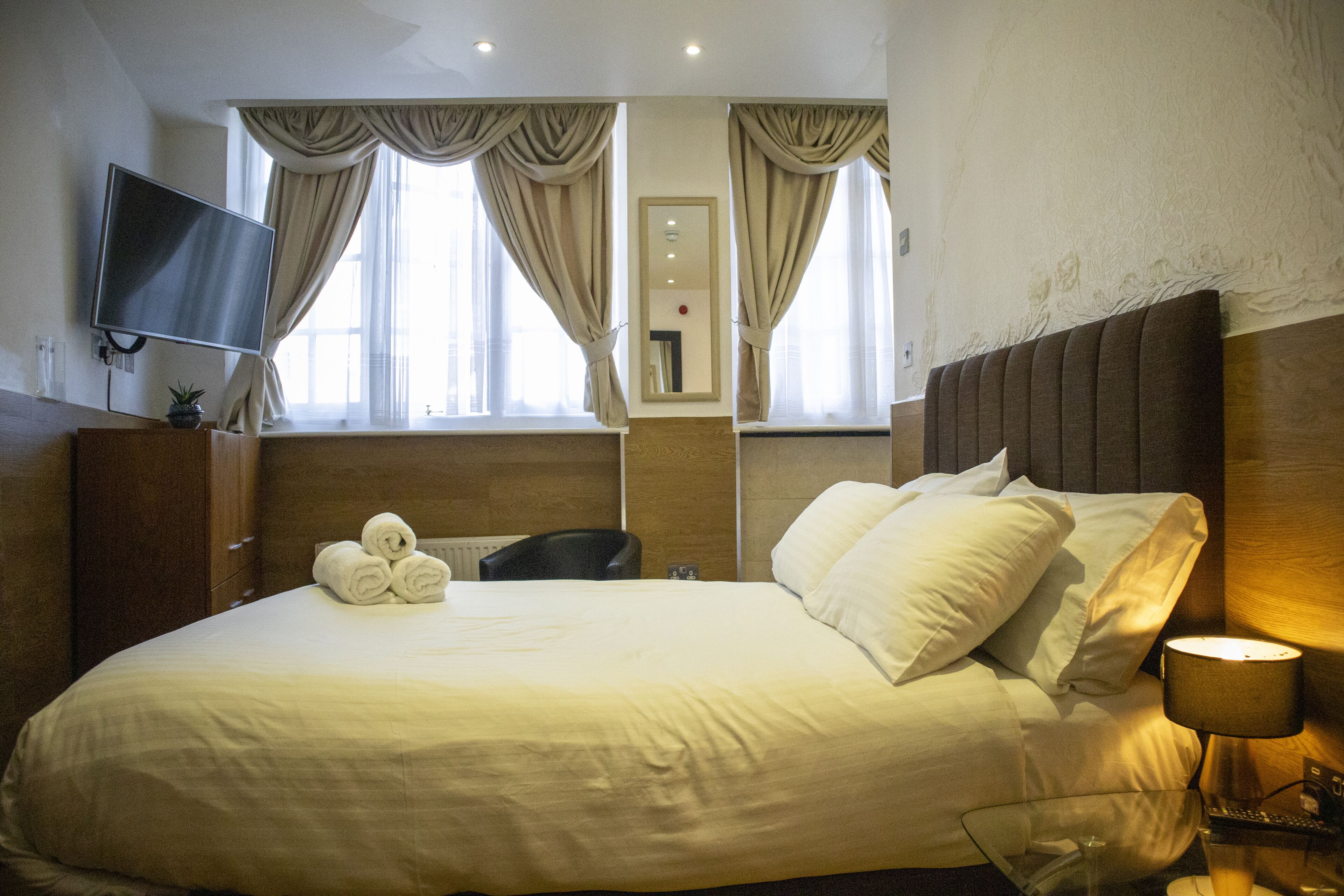 Una camera d'hotel con un letto grande, una TV a schermo piatto montata a parete, una scrivania con una lampada e una finestra con tende.
