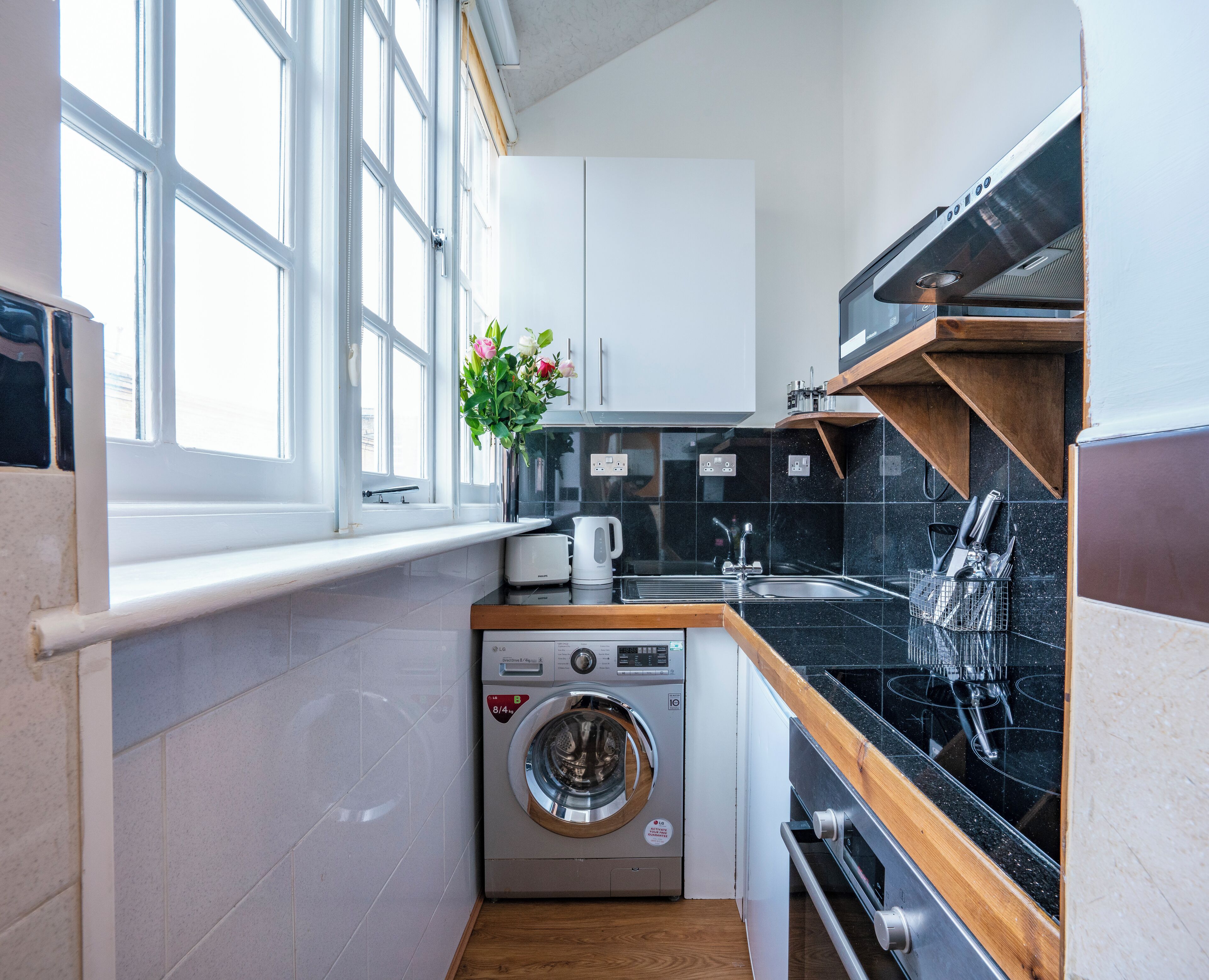 Cocina compacta con lavadora y secadora integradas, encimera de madera y ventana que proporciona luz natural.