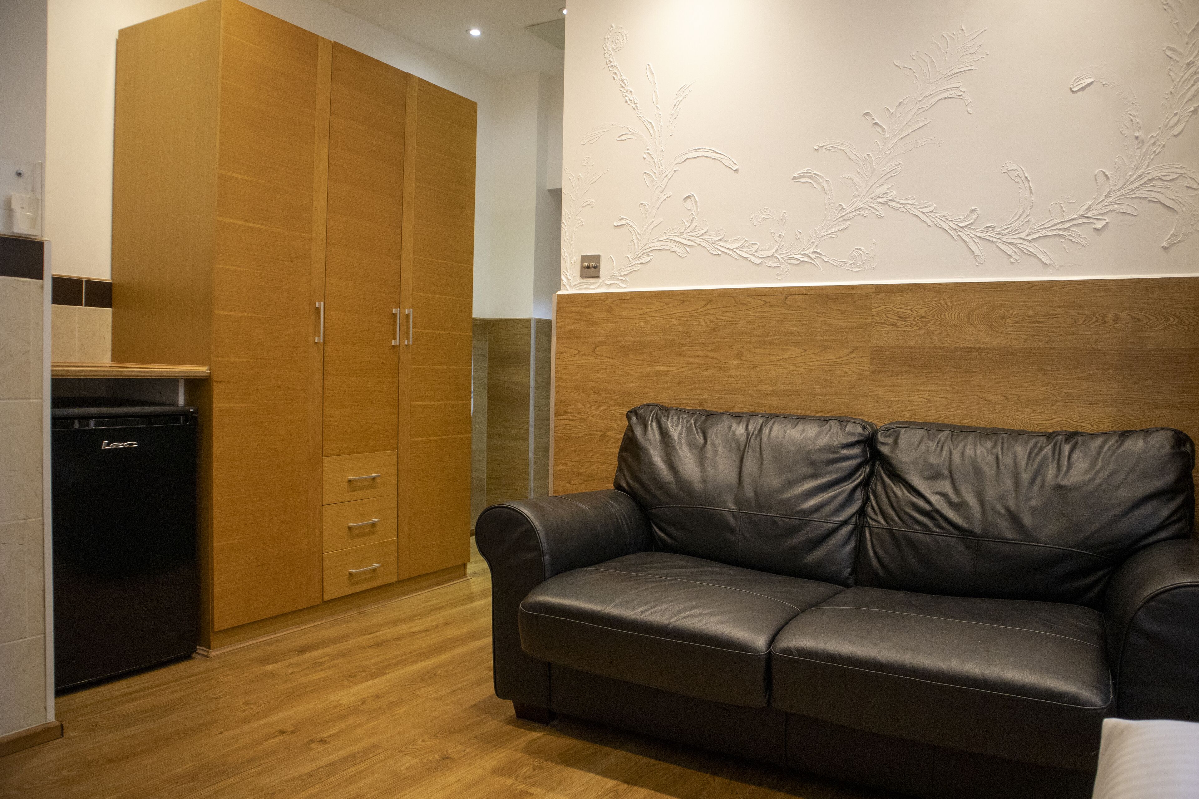 A modern kitchen with wooden cabinets, a black refrigerator, and a black leather sofa.