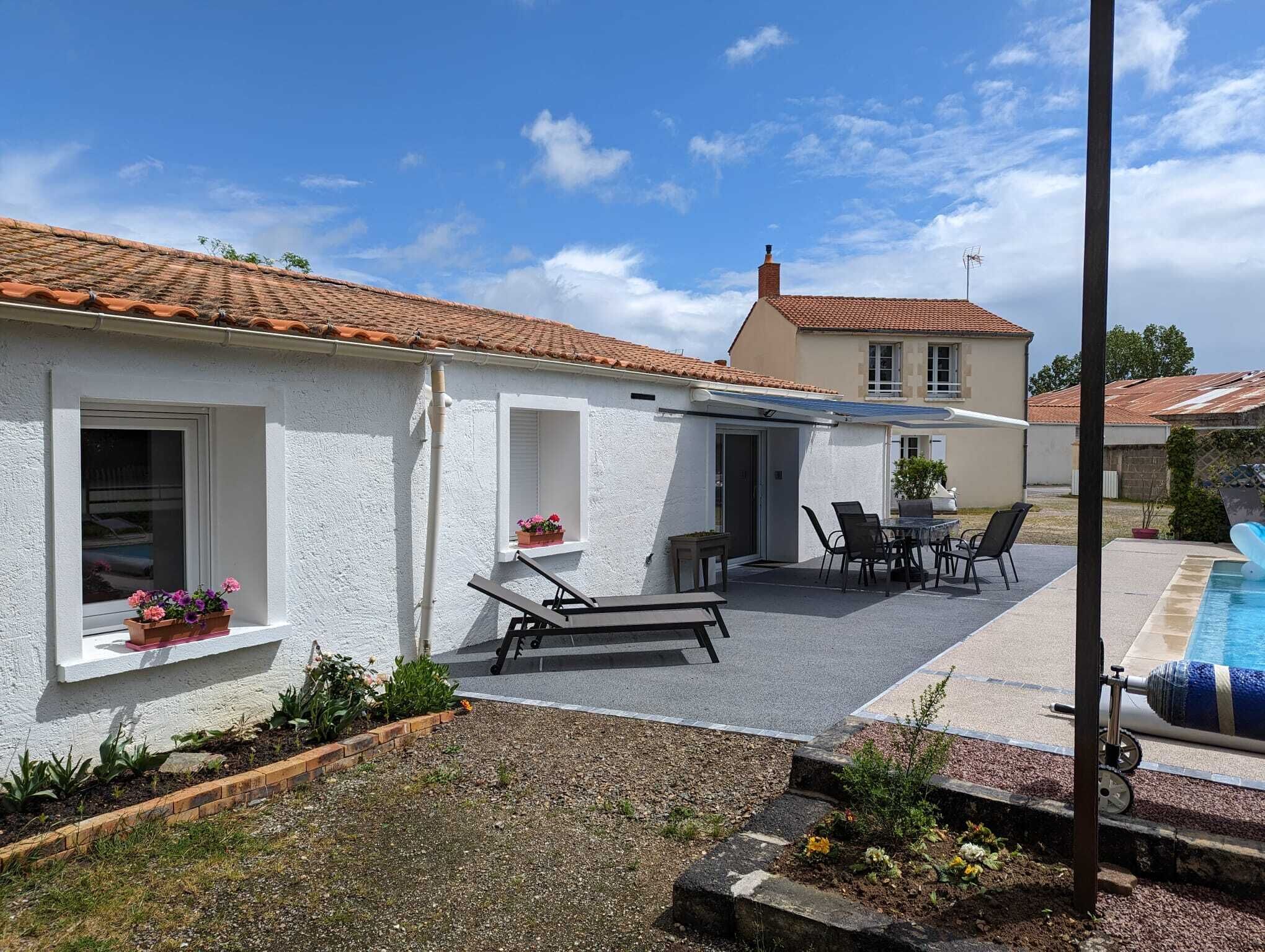 A white house with a tiled roof, a patio with a table and chairs, and a swimming pool.