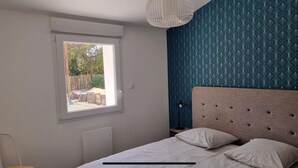 Een slaapkamer met een bed, een raam en een blauwe, patroonrijke wand.
